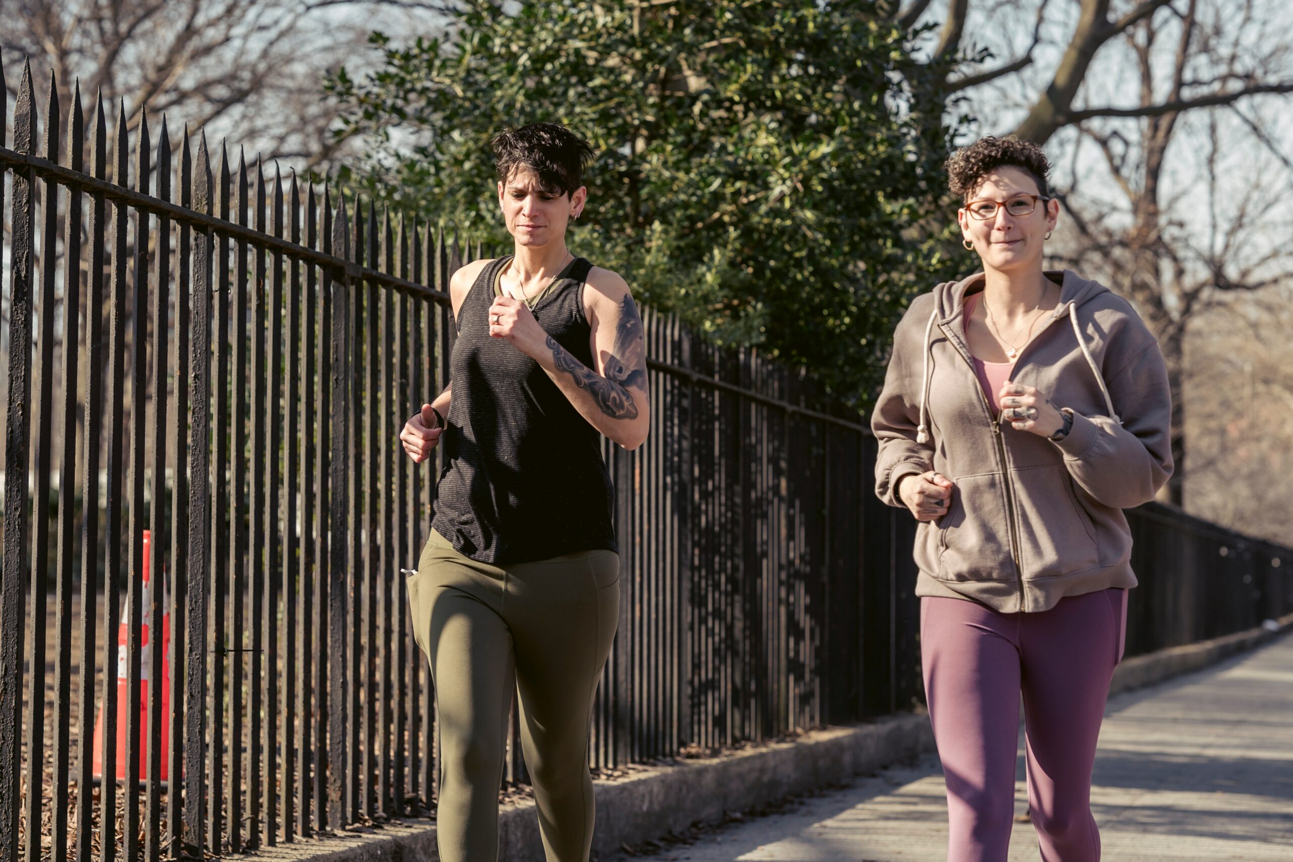 Two women jogging alongside a tall iron fence