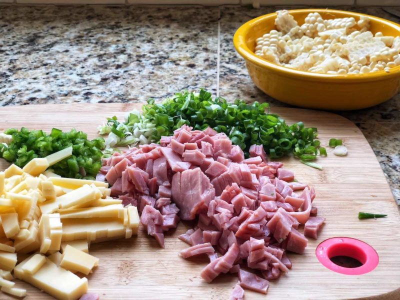 The ingredients for the healthy frittata recipe, gruyere, chives, pepper, and ham sitting on a cutting board