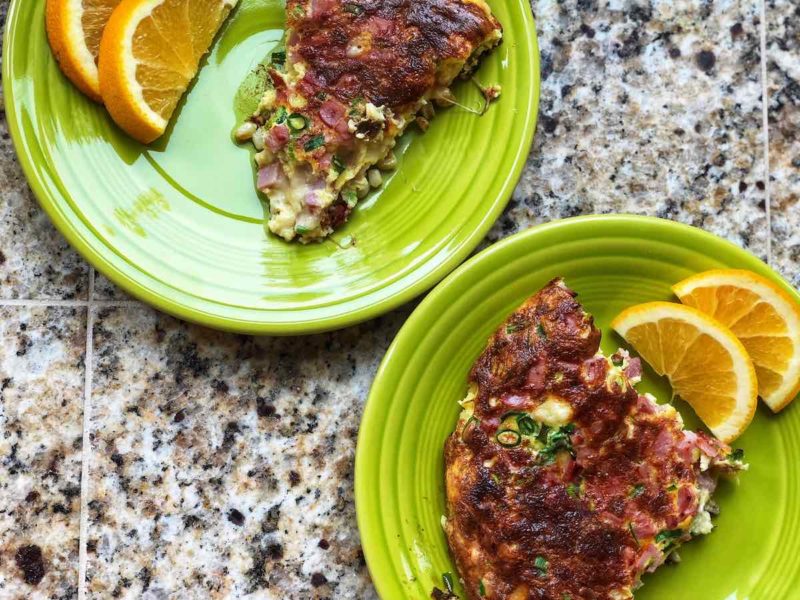 A picture of two slices of the frittata on two green plates, with slices of orange