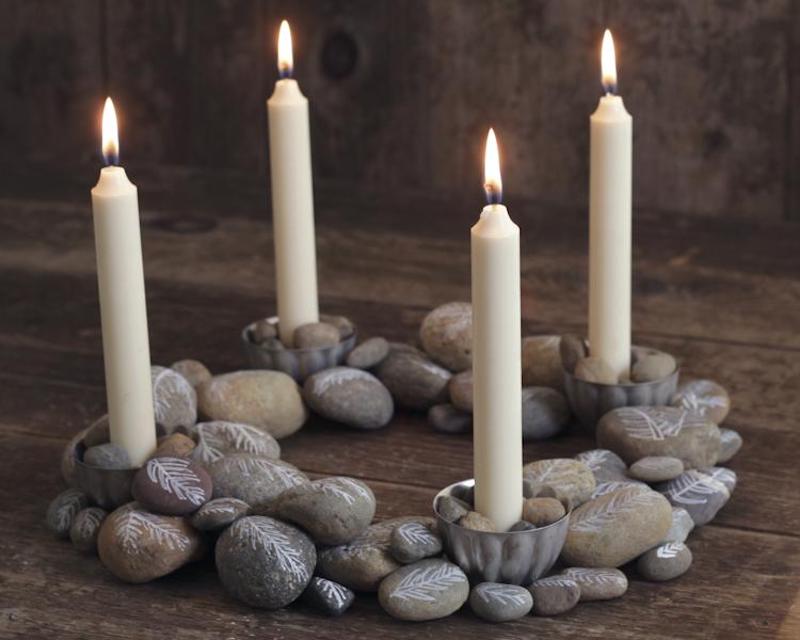 An advent wreath made out of stones with four lit candles placed in it