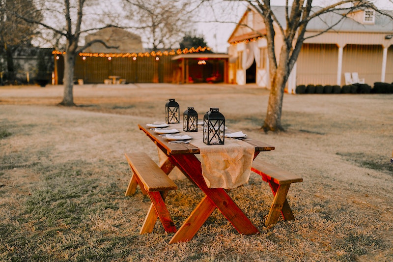 A picnic table outdoors, with dining settings. In front of a house and barn.