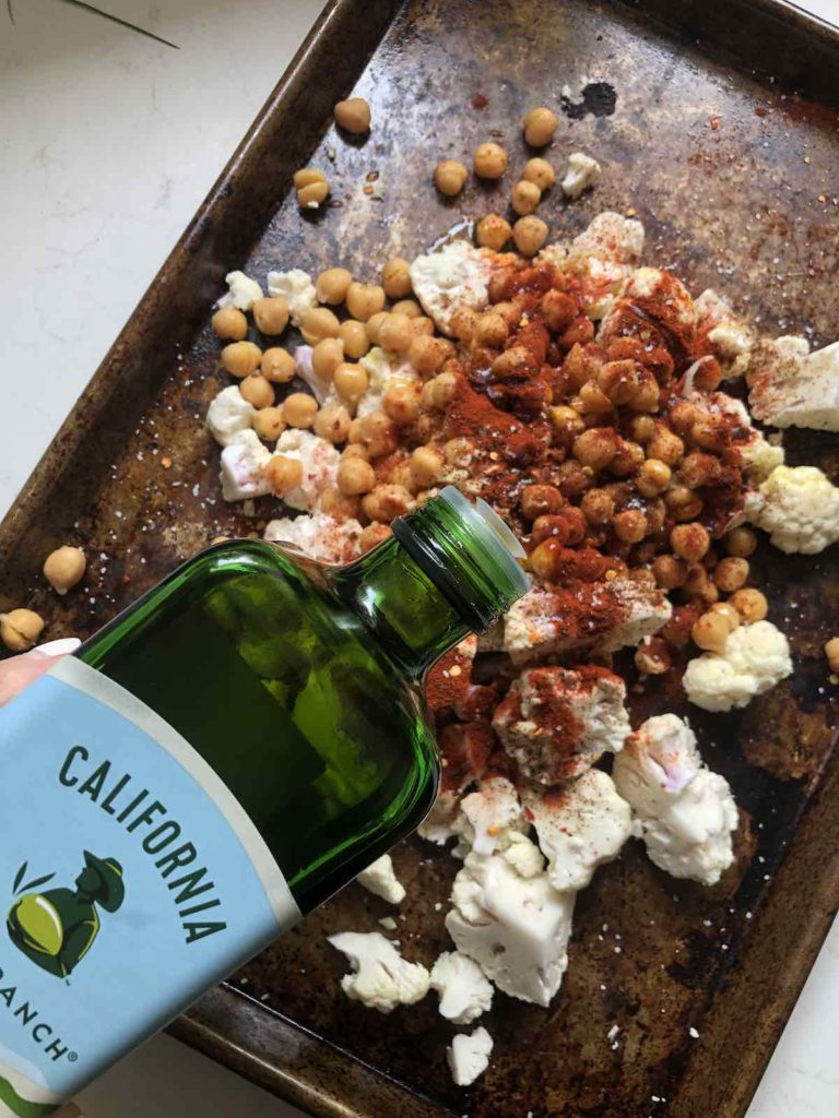 Olive oil and spices being added to a sheet pan of roasted cauliflower