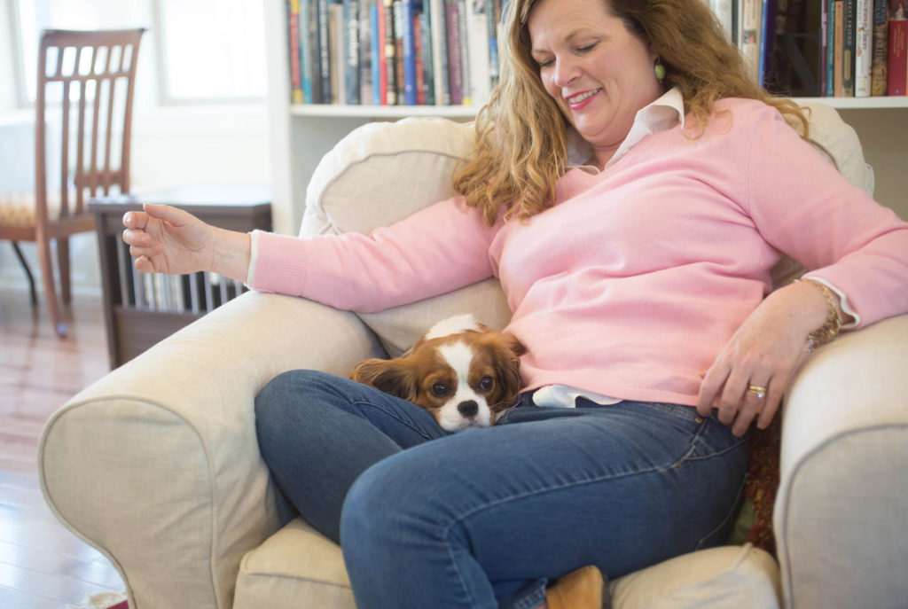 Biography page photo of Marie Bostwick sting in chair with her dog 