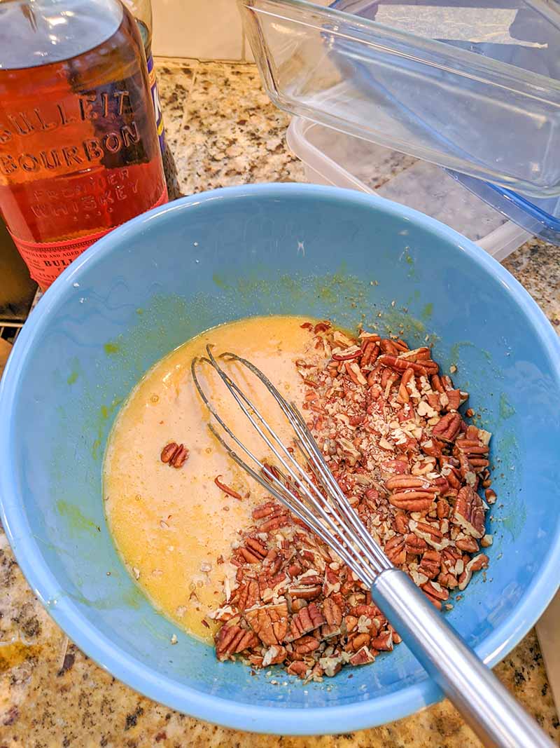 The wet ingredients for the pecan pie and the crushed pecans in a blue mixing bowl