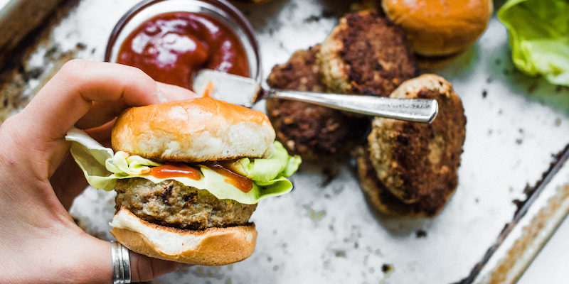 One of the sliders from the Turkey Sliders Recipes being held above a metal tray with ketchup and patties