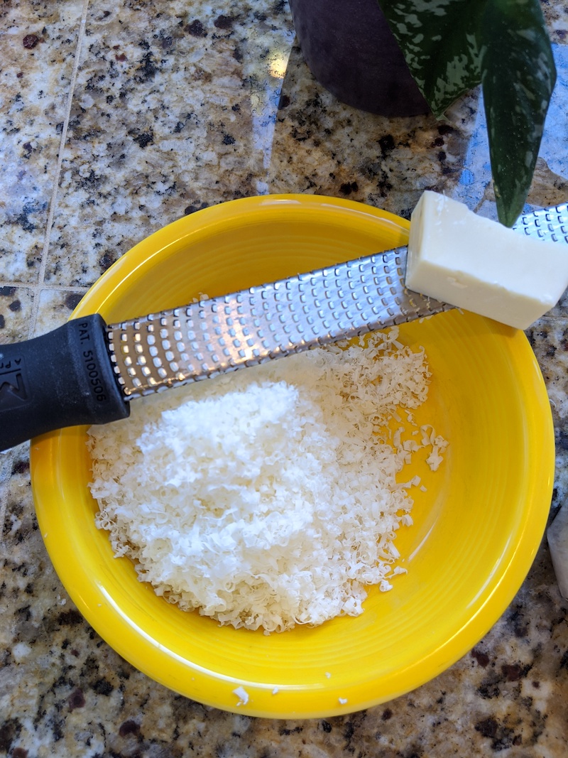 A yellow bowl with parmesan cheese being grated into it.