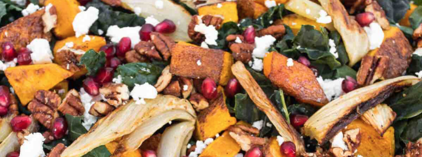 A kale salad with butternut squash, pomegranate seeds, and feta cheese.