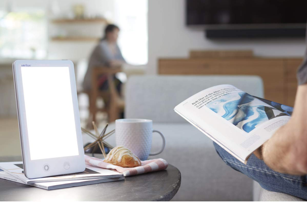 A woman sits reading near a Season Affective Disorder treatment light