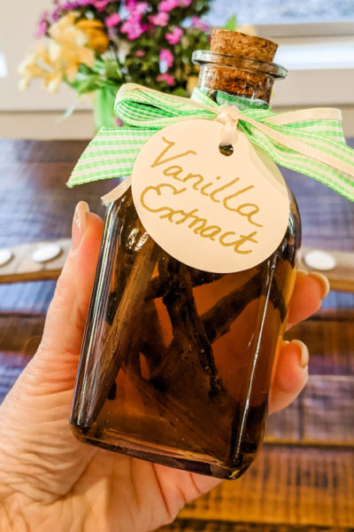 A hand holding the easy homemade vanilla extract in a bottle with a bow and label