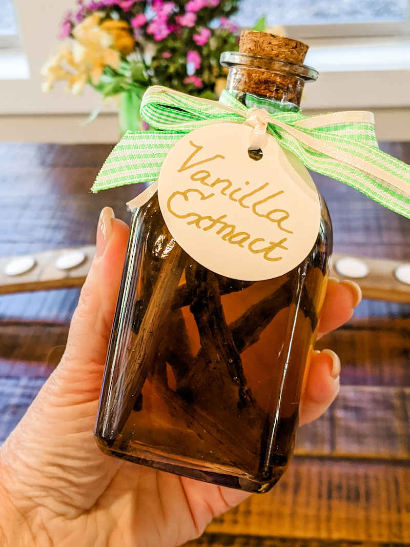 A hand holding the easy homemade vanilla extract in a bottle with a bow and label