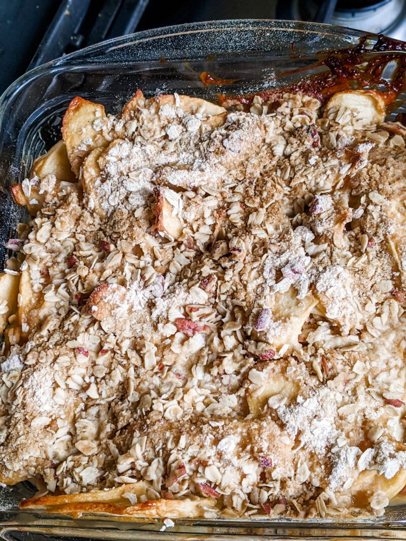 The baked Apple Crisp Recipe in a glass baking dish atop a stove - all baked in one pan for an easy fall recipe