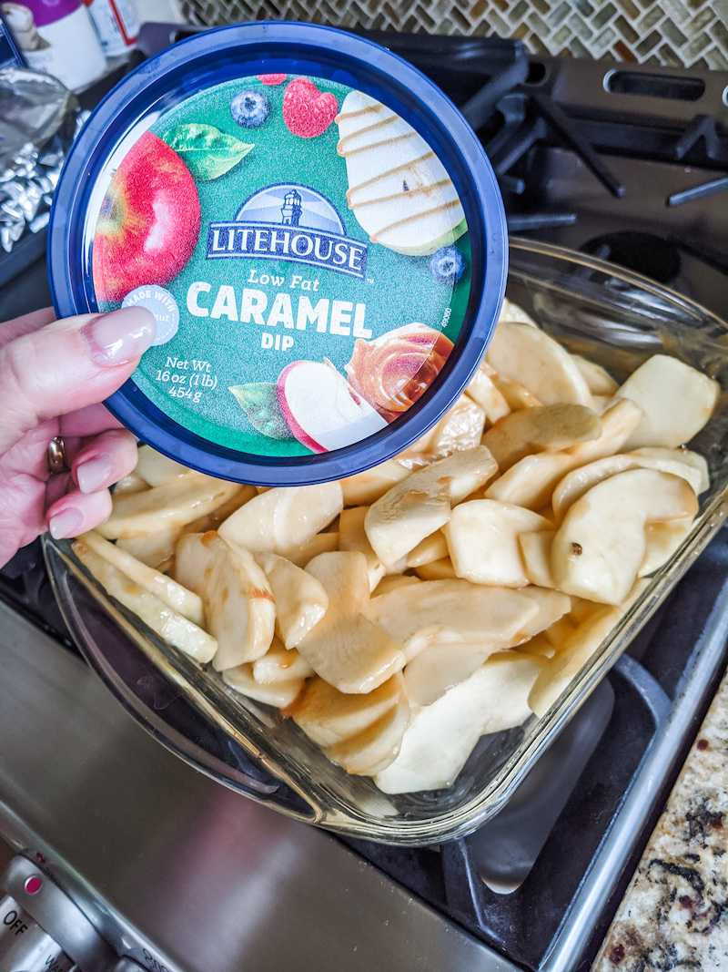 The container of Low fate caramel dip held above the pre-baked Healthy Apple Crisp Recipe