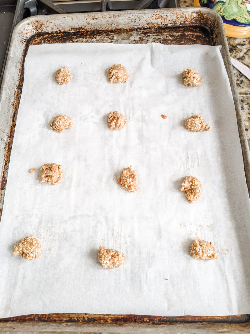 A dozen teaspoon-sized balls of benne wafer batter sitting on a tray lined with parchment paper