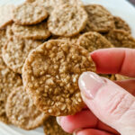 A plate of benne wafers and a hand holding one up