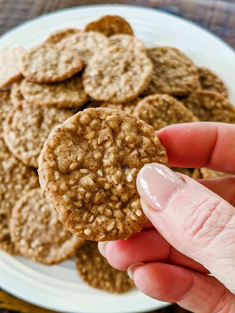 A plate of benne wafers and a hand holding one up