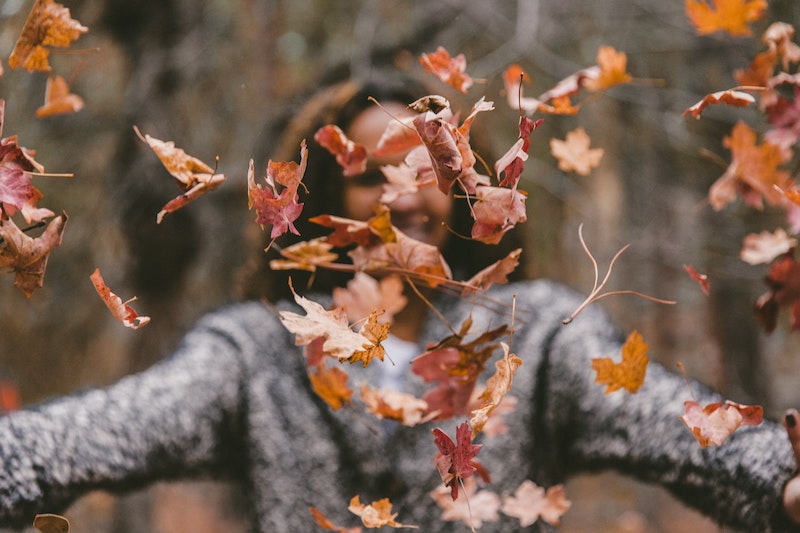 A woman in a sweater throwing leaves in the air