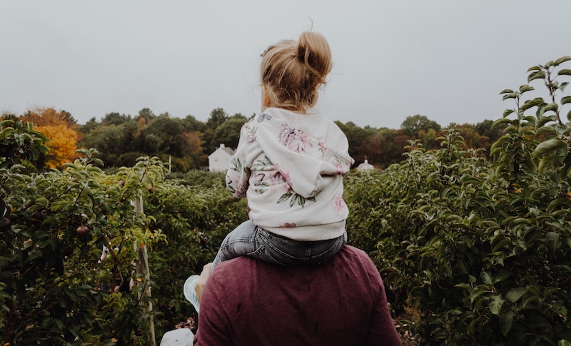 A man with his daughter on his shoulders, walking through a pumpkin patch