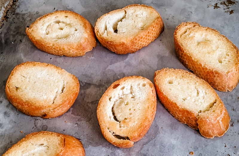 The baked pieces of baguette sitting on a pan