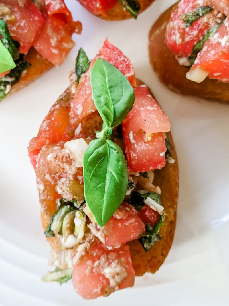 A piece of my easy tomato bruschetta topped with basil 