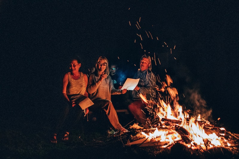 Two women and a man enjoying a fall activity of a bonfire and singing