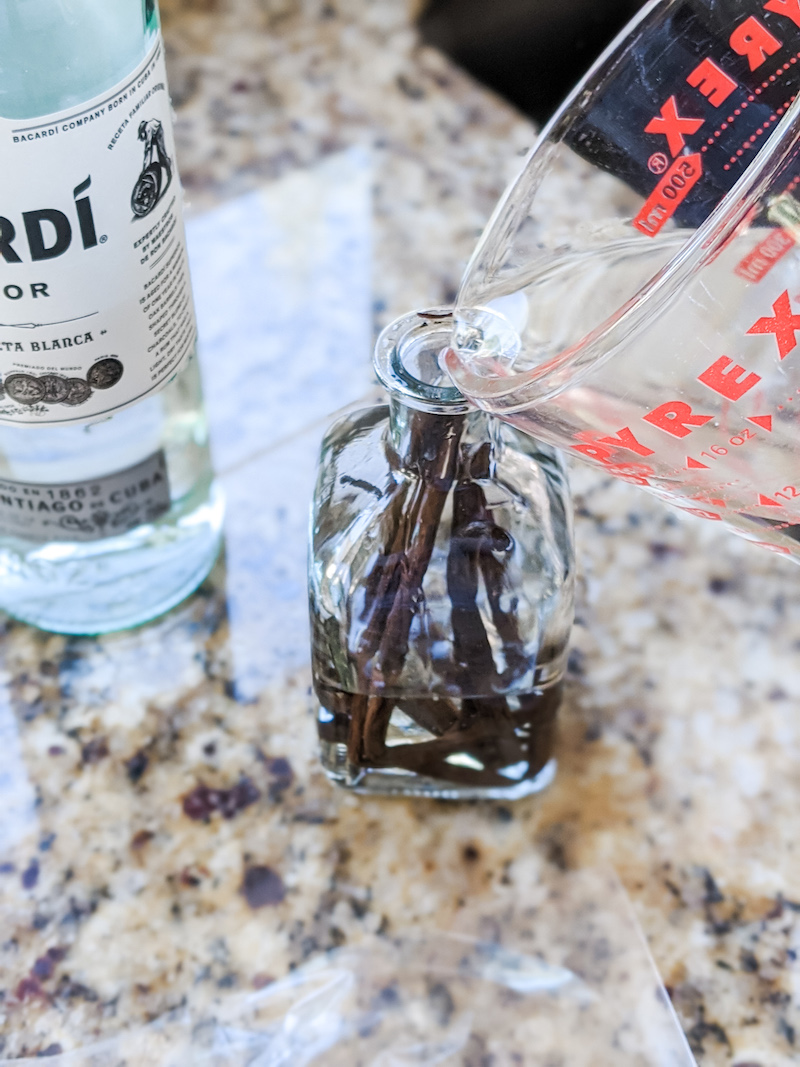 A measuring cup pouring rum into the bottle with vanilla beans