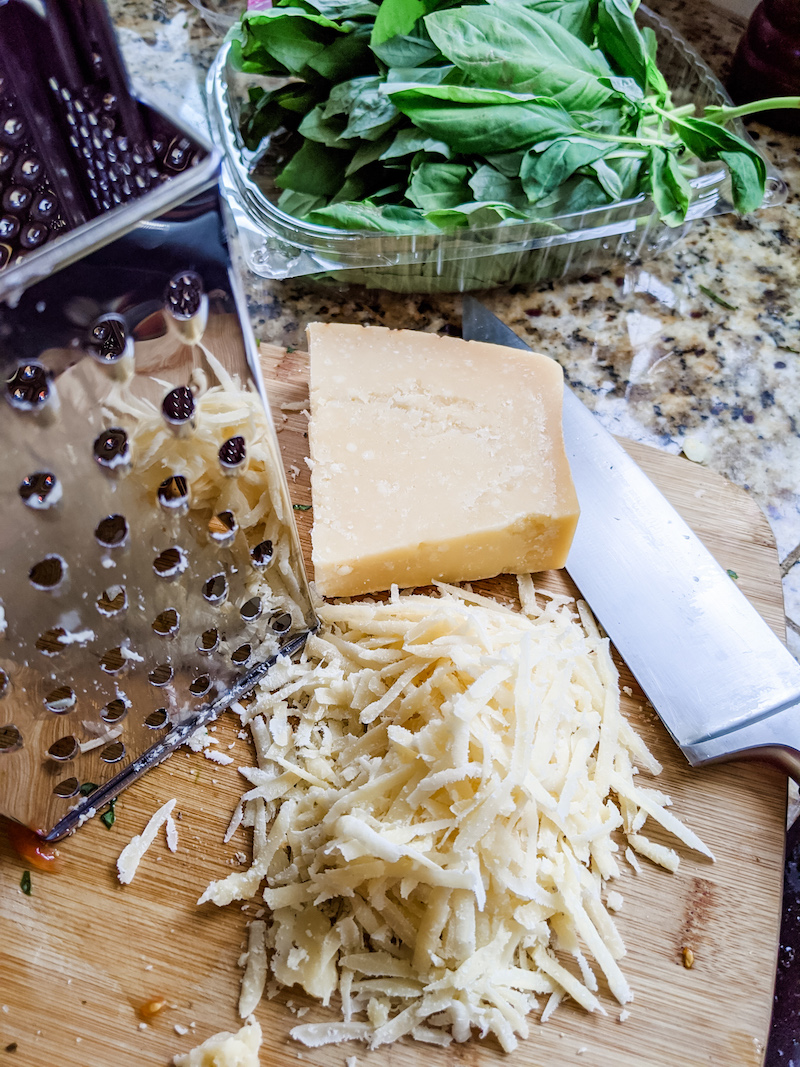 A pile of grated parmesan cheese next to a chunk of it and a grater.