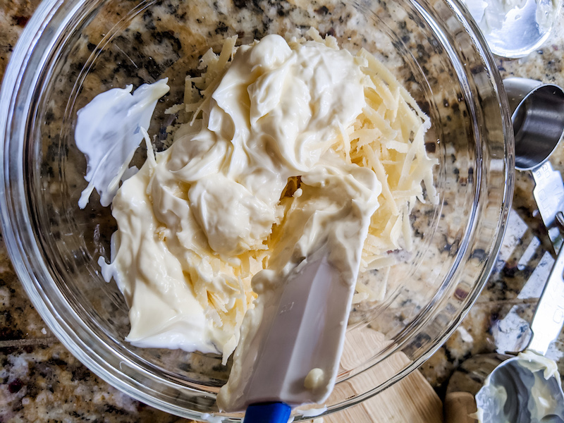 A clear bowl containing a mixture of mayonnaise and grated cheese