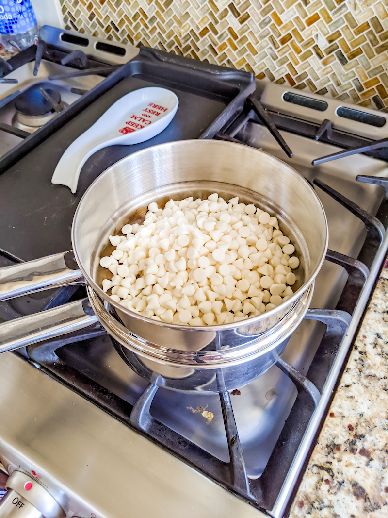 A double boiler atop a stove top with white chocolate chips. 