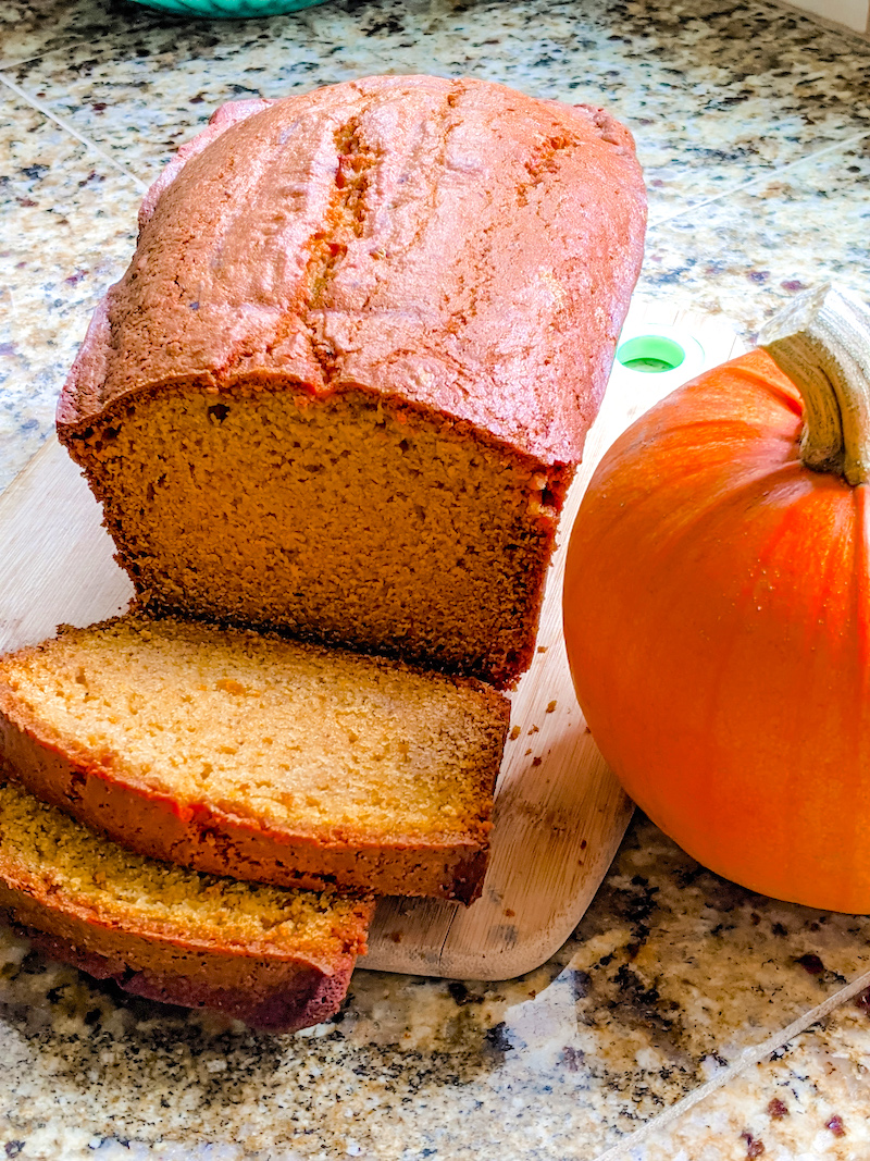 The Easy Homemade Pumpkin Puree used in a pumpkin bread, which sits, sliced, next to a pumpkin