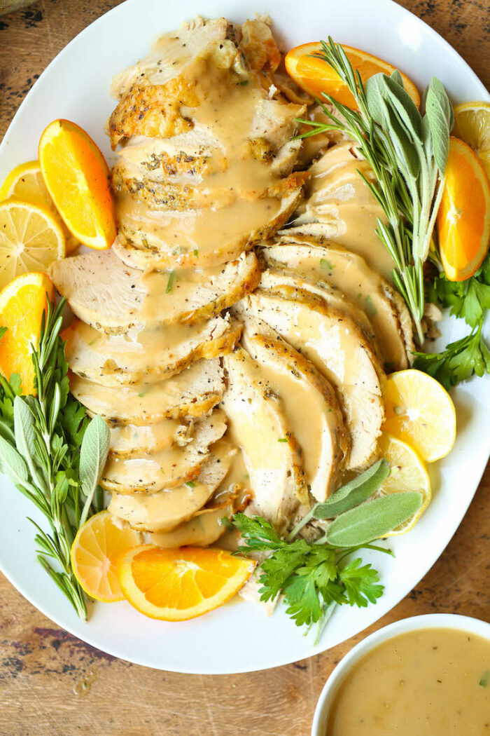 A serving dish with the turkey topped with gravy alongside herbs an oranges