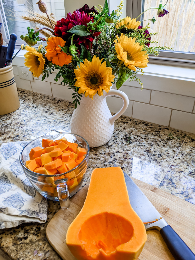 A butternut squash cut in half with the other half cubed, in a bowl.