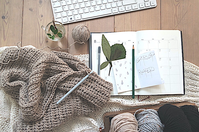 A shot from above picture of yarn, blankets, a keyboard, and notebook.