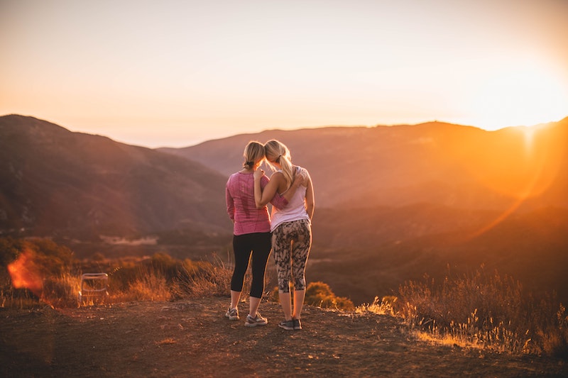 Two women leaning against each other while watching a sunset