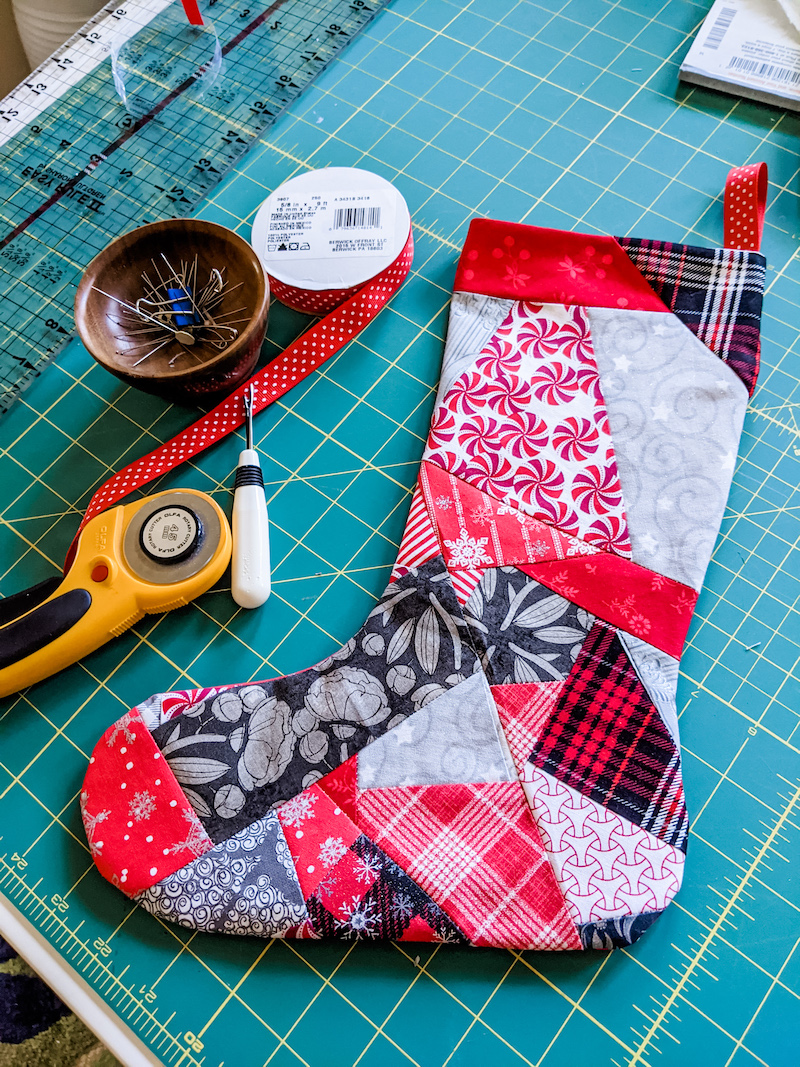 A finished Easy Patchwork DIY Christmas Stockings surrounded by the tools used to make it.
