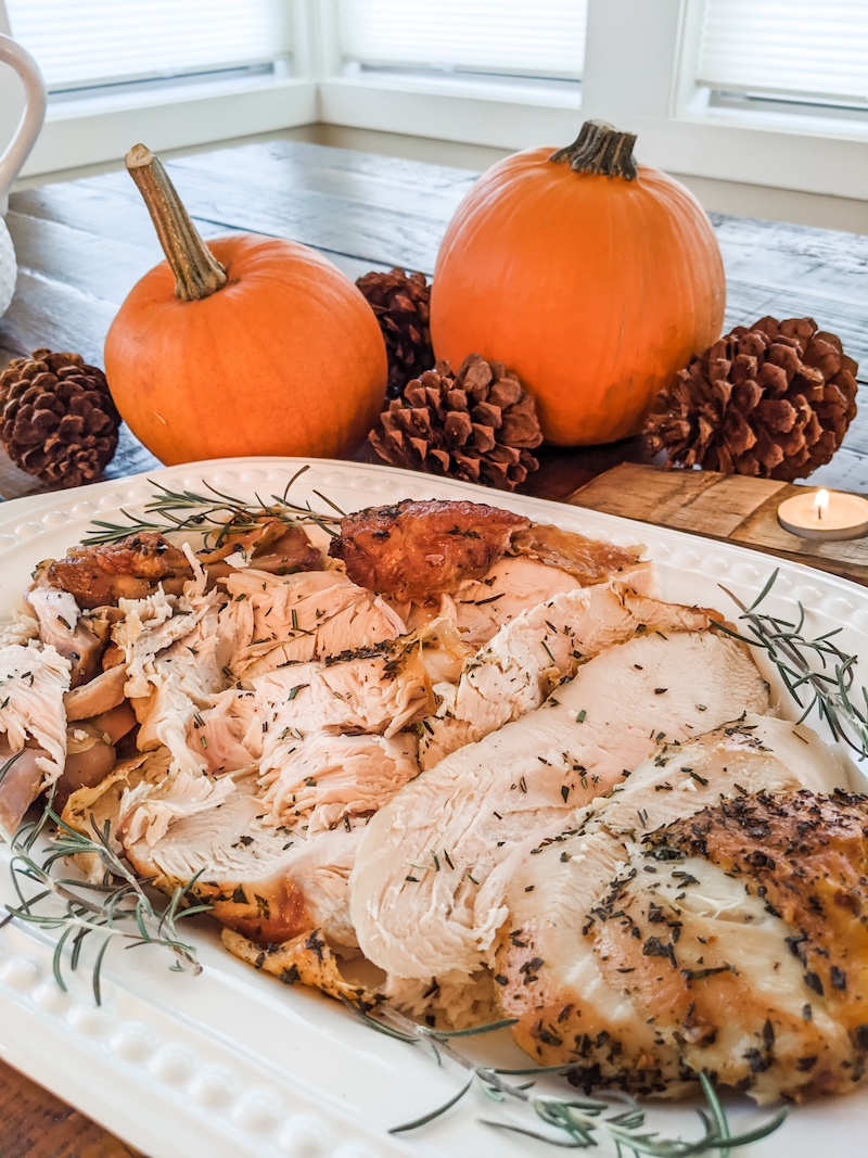 The finished and sliced small scale oven roasted turkey breast on a platter with a pumpkin centerpiece behind