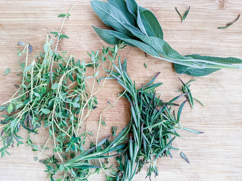 Sprigs of fresh rosemary, sage, and thyme on a wooden board