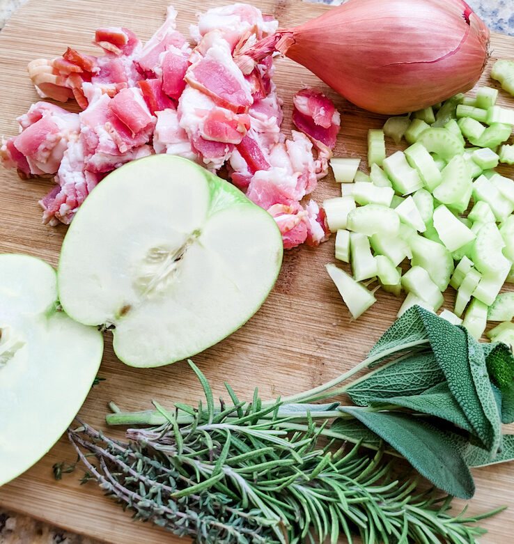 The ingredients for the best flavorful and moist turkey dressing - apple, bacon, herbs, shallots - on a cutting board