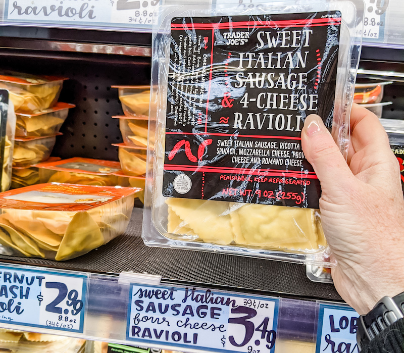 A hand pulling a package of fresh ravioli off a shelf. 