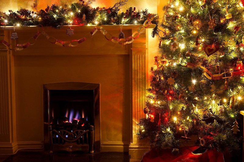 A fireplace decorated with Christmas garland next to a lit and decorated tree - the perfect place for the best Hallmark Christmas Movies to Watch in 2020