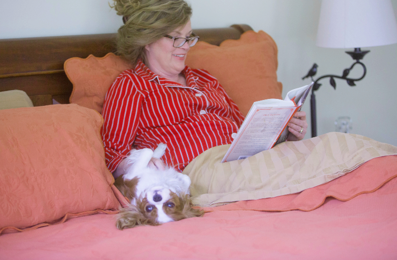 Marie sitting in bed alongside her dog, reading a book.