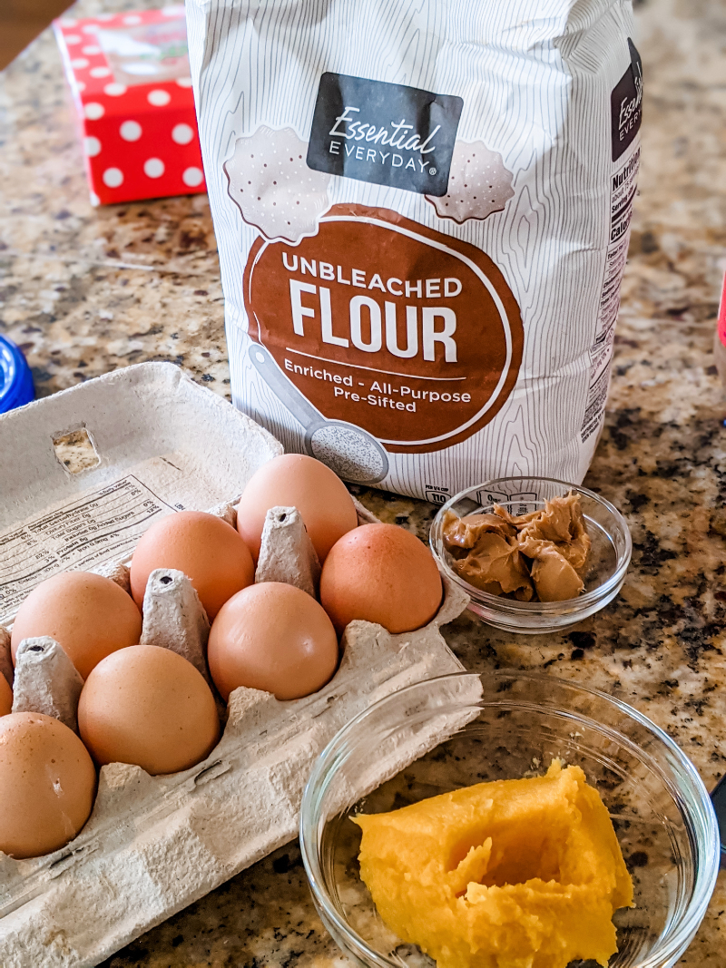 The ingredients for the dog treat recipe laid out - eggs, flour, pumpkin, and peanut butter.