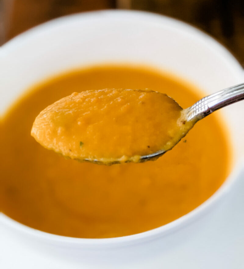 A spoon with some of the Carrot Pear Soup held above its bowl