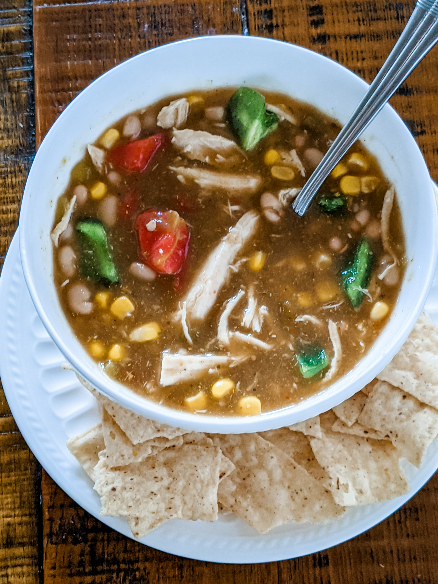 The finished slow cooker chili in a bowl on top of a plate, with some tortilla chips on the side