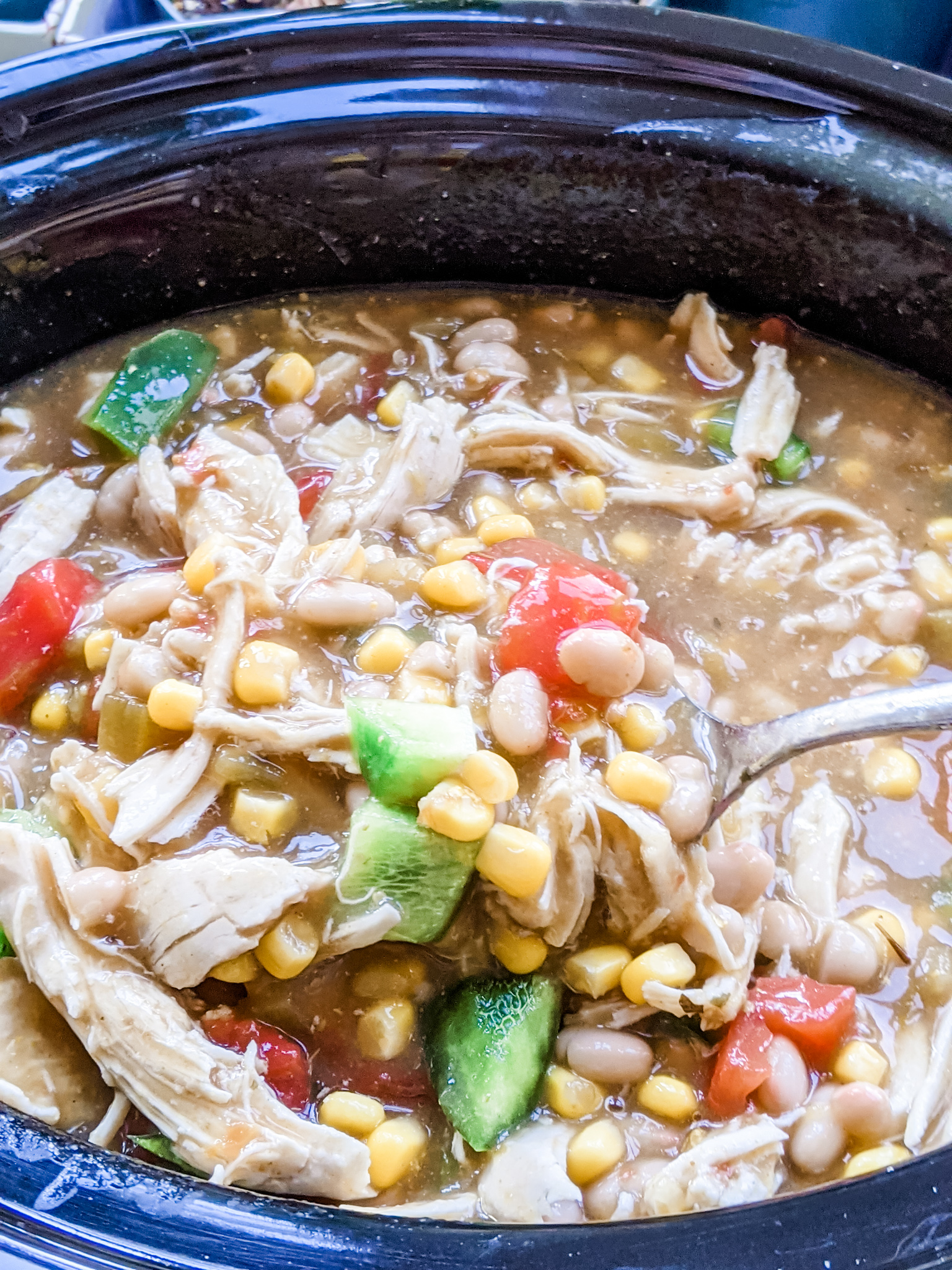 The Easy Weeknight Chicken Chili in the slow cooker, with a spoon being dipped into it