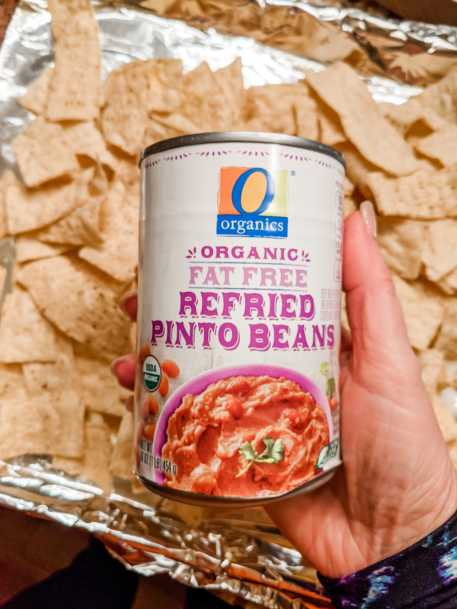 A can of refried beans held above a try filled with tortilla chips