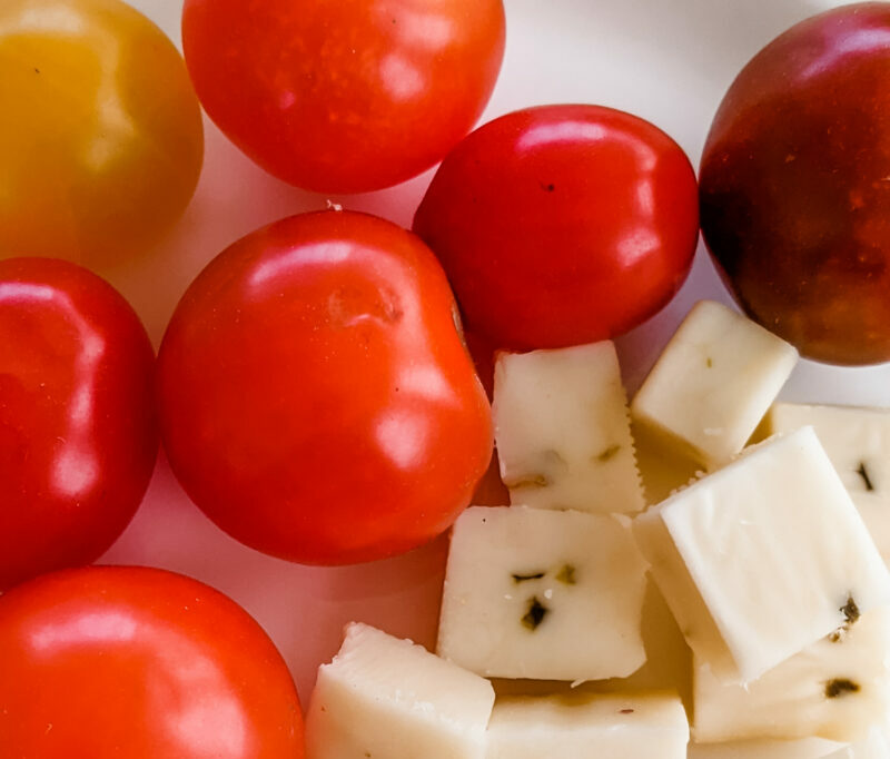 Cherry tomatoes and cubed pepperjack cheese together on a white plate.