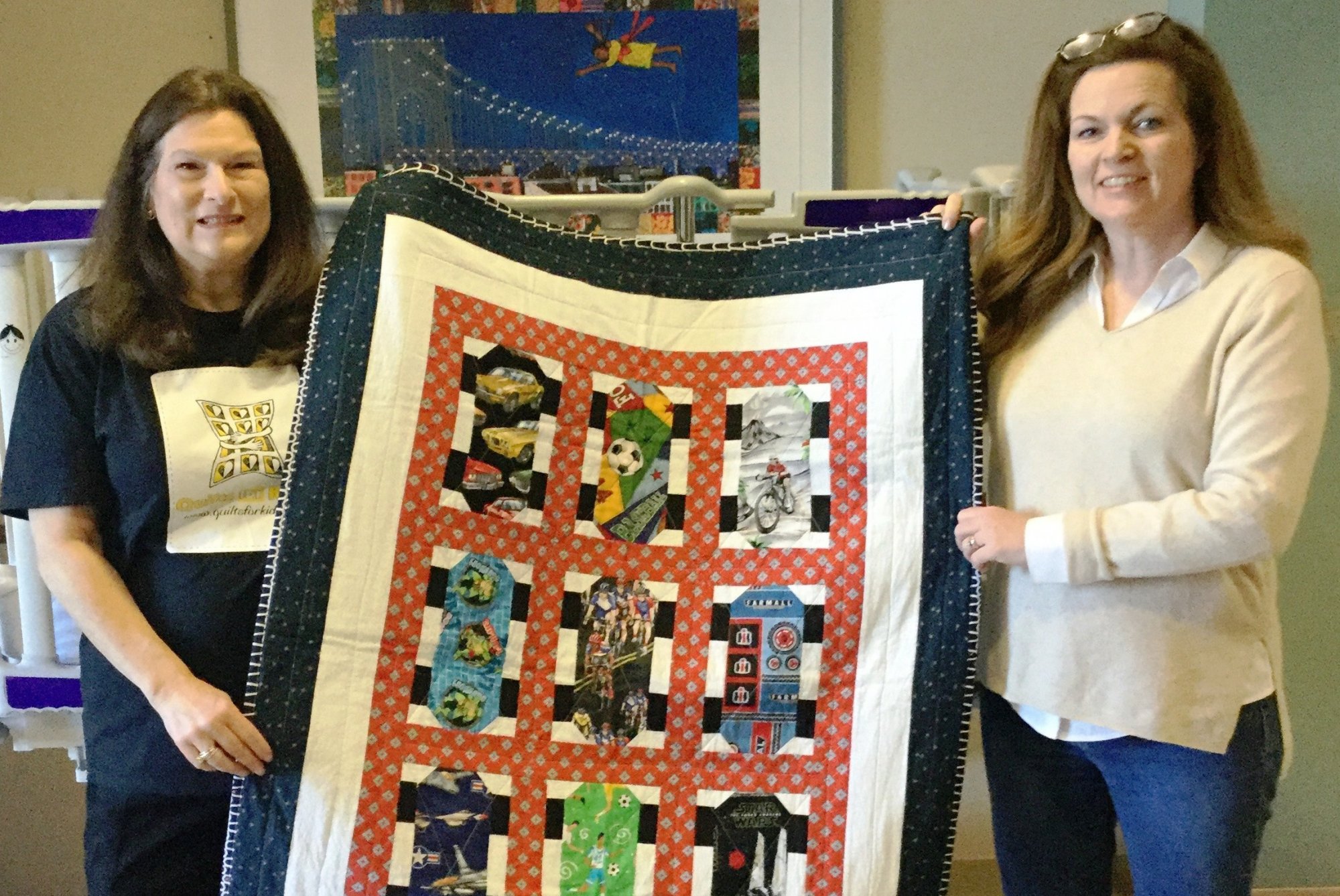 Marie and a volunteer stand, holding a quilt