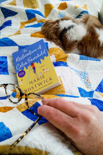 A copy of The Restoration of Celia Fairchild on a quilt, with Marie's sleeping dog in the background.