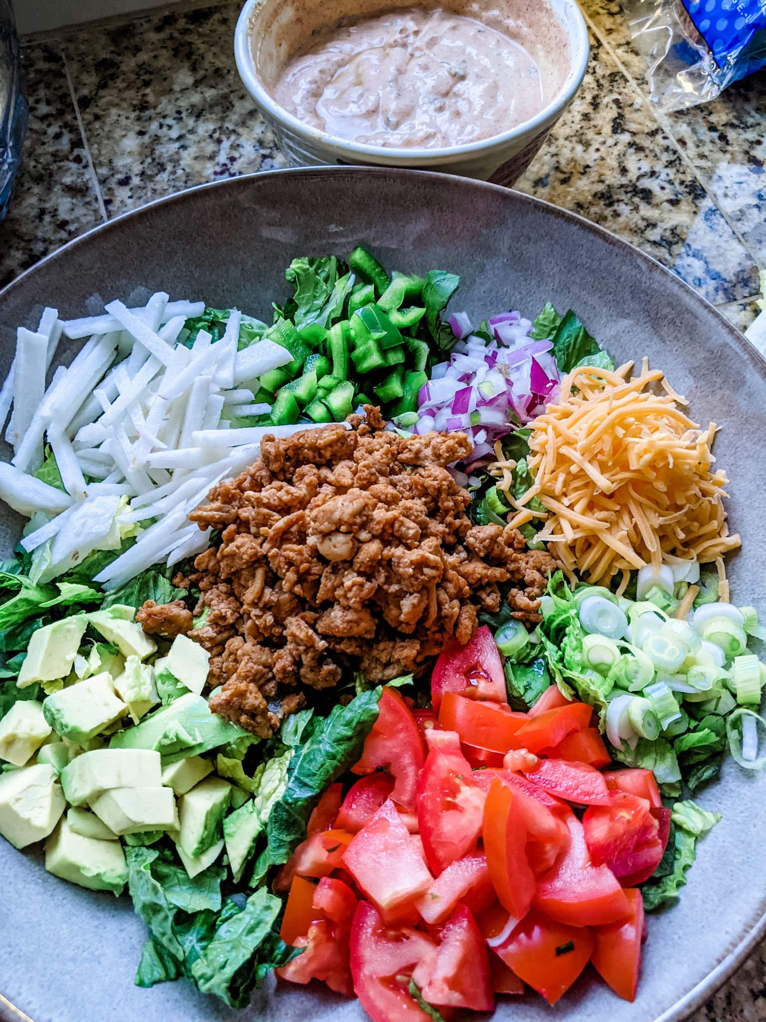 Marie's finished Chicken Taco Salad in a bowl, with the buttermilk ranch dressing behind it.