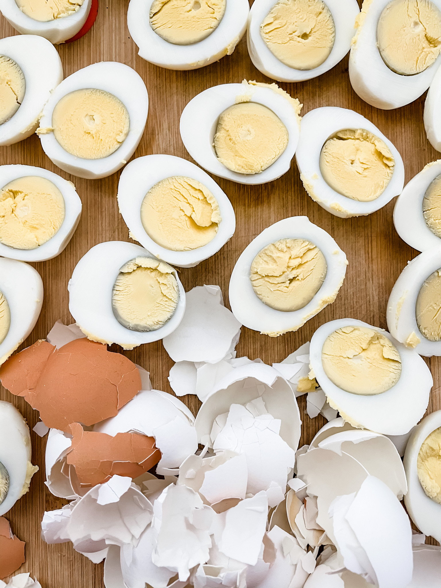 Shelled and halved hard-boiled eggs and their cracked shells on a wooden surface.